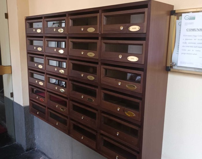 Una bacheca in legno scuro con numerosi caselle postali e targhette dorate all'ingresso di un condominio.